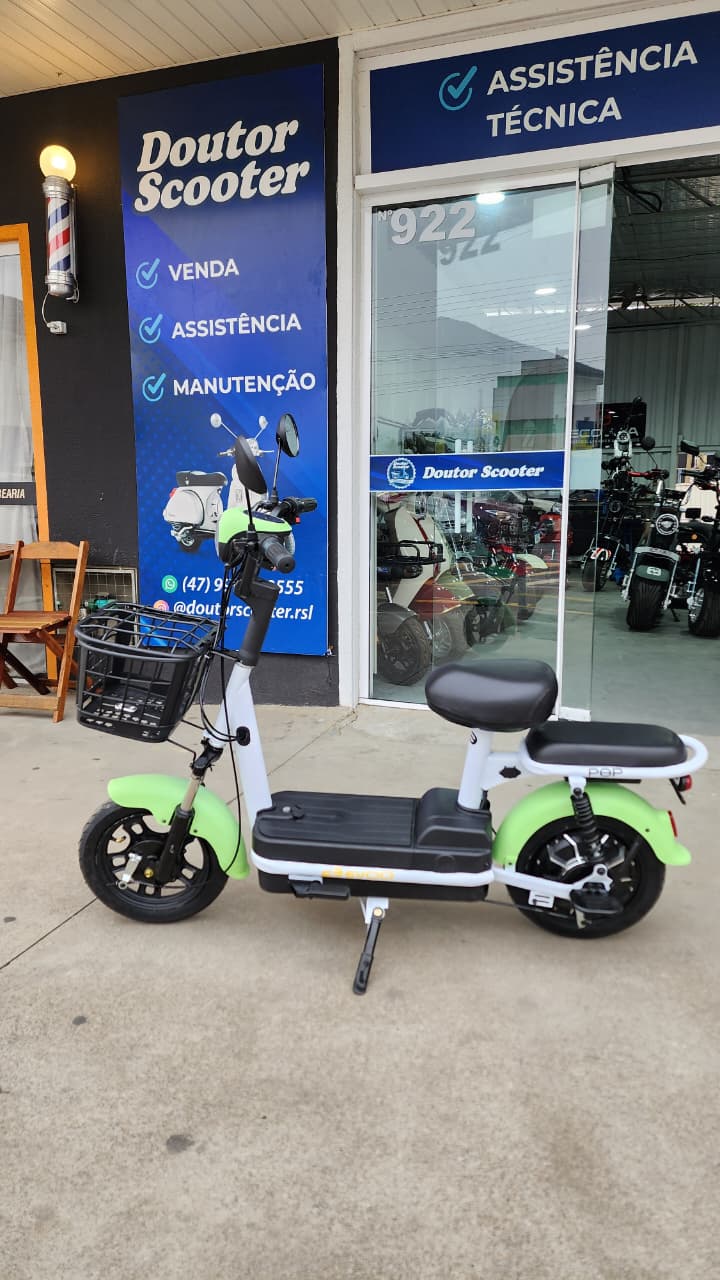 Scooter elétrica verde e branca com cestinha em frente à Doutor Scooter